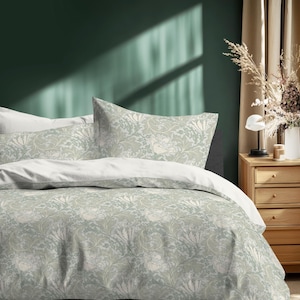 May include: A bed with a floral patterned duvet cover and pillowcases in shades of green and white. The bedding is set against a dark green wall. A wooden nightstand with a lamp and vase of dried flowers is visible.