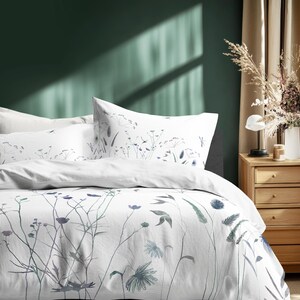 May include: White bedding set with a botanical design featuring blue and green floral and leaf patterns. The set includes a duvet cover and pillowcases. The bedroom has a green wall and a wooden nightstand.
