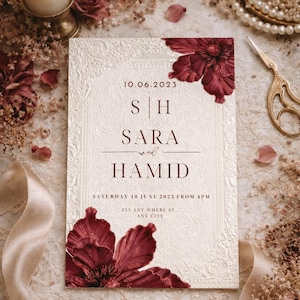 May include: A cream-coloured wedding invitation with embossed floral patterns and burgundy floral accents. The invitation includes the names "Sara and Hamid" and event details. A lit candle, pearls, and scissors are in the background.