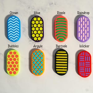 May include: Eight oval-shaped textured silicone charms arranged in two rows. Patterns include Ocean, Hive, Ripple, Raindrop, Bubbles, Argyle, Barcode, and Wicker, each featuring distinct color combinations like blue, yellow, orange, purple, green, and red.