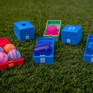 May include: A collection of small plastic storage containers in red, blue, and green, some open and some closed. Inside the containers are various colorful items, including swirled spherical balls and translucent rectangular blocks.