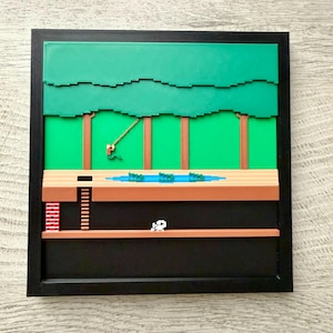 Puede incluir: Obra de arte enmarcada que representa una escena de videojuego pixelada. La obra presenta un dosel de árboles verdes, troncos de árboles marrones, un estanque azul con nenúfares verdes y un personaje blanco. El marco es negro.