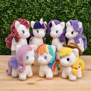 May include: A collection of seven crocheted pony figurines. Each pony has a white body, colorful manes and tails, and blue eyes. Some ponies have horns, and one wears a cowboy hat. The ponies are arranged in a group.