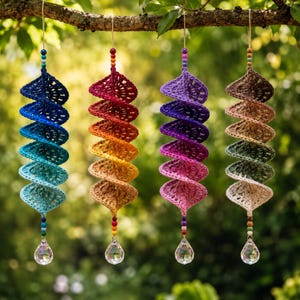 Peut inclure: Quatre ornements en crochet en forme de spirale suspendus à une branche. Chaque ornement présente un dégradé de couleurs, incluant le bleu, l'orange-jaune chaud, le violet-rose et des tons terre, avec des perles et un prisme en cristal.