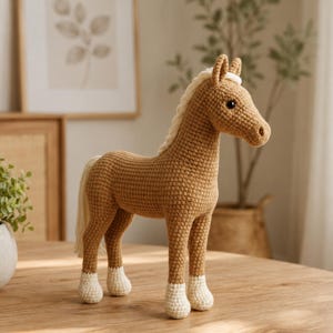 May include: A tan crochet horse toy featuring a cream-coloured mane and tail, with four cream-coloured hooves. The horse has dark brown safety eyes and a stitched nose detail, crafted with a textured yarn stitch pattern throughout its body.