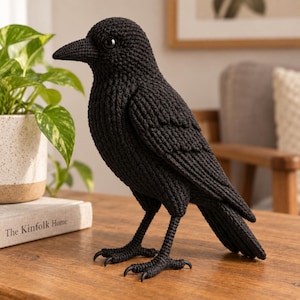 Op de afbeelding: Een handgemaakt zwart gehaakt kraai-figuurtje met een lichaam van getextureerd garen, een puntige snavel en donkere glanzende ogen. De vogel staat op twee dunne, beweegbare poten met gedetailleerde klauwen en toont een nauwkeurig haakpatroon.