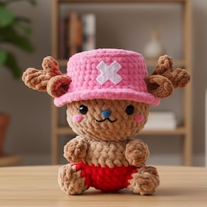 May include: A handmade crochet plush toy of a cartoon character. The plush has a brown body, red shorts, and a pink hat with a white cross. It has brown antlers, a blue nose, and pink cheeks. The toy is sitting.