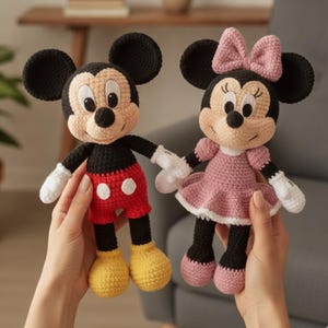 Puede incluir: Dos muñecos de ganchillo que representan a Mickey y Minnie Mouse. Mickey tiene orejas negras, cara beige, pantalones cortos rojos con botones blancos y zapatos amarillos. Minnie lleva un vestido rosa con lazo a juego y zapatos rosas.