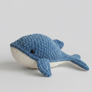May include: A handmade blue and white crochet whale plush toy. The whale has a textured, chunky stitch pattern, black eyes, and a white belly. The fins and tail are also blue.