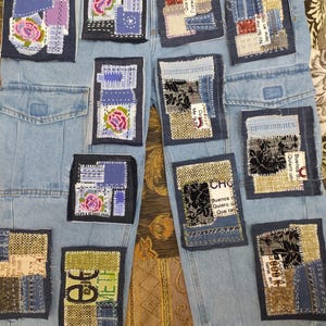 Könnte beinhalten: Hellblaue Jeanshose mit mehreren aufgenähten Stoffflicken. Die Flicken zeigen florale Designs, Text und verschiedene Texturen in Blau-, Rosa- und Grüntönen. Die Hose hat Taschen und einen ausgefransten Saum.