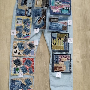 May include: Light blue denim jeans featuring eleven distinct rectangular patches numbered one through eleven. Each patch displays a unique collage of fabric scraps, including denim, patterned textiles, and embroidered elements, stitched onto the legs.
