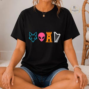 Peut inclure: T-shirt noir avec un motif graphique coloré représentant une tête de renard, une tête d'extraterrestre, une pièce d'échecs et une harpe. Le motif est en bleu, rose, orange et blanc. Le t-shirt est de style décontracté.