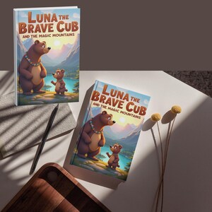 Peut inclure: Deux exemplaires d'un livre pour enfants intitulé "Luna the Brave Cub and the Magic Mountains". La couverture présente un ours brun et un ourson dans un paysage de montagne. Le titre est en grandes lettres oranges sur fond de ciel bleu.