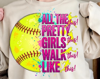 Può includere: Una felpa color crema con una grande grafica di softball. Il testo recita "ALL THE PRETTY GIRLS WALK LIKE THIS!" in rosa e giallo. La palla da softball è gialla con cuciture rosse e spruzzi di vernice colorati.