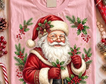 Può includere: Una t-shirt rosa chiaro con un'illustrazione grafica di Babbo Natale che indossa un abito rosso con bordo in pelliccia bianca e un cappello abbinato. Babbo Natale è circondato da una ghirlanda di rami di pino, bacche di agrifoglio e pigne.
