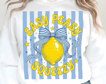 Può includere: Una felpa bianca a girocollo con una stampa grafica di un limone giallo brillante legato con un fiocco a righe blu e bianche. Il testo "EASY PEASY SQUEEZY" è stampato in giallo sopra e sotto il limone, circondato da piccole stelle blu e gialle.