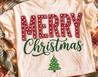 Può includere: Una t-shirt color crema con la scritta rossa MERRY in un carattere grassetto a pois, seguita dal testo verde in corsivo Christmas e una piccola grafica di un albero di Natale verde con pois bianchi centrata sotto il testo.