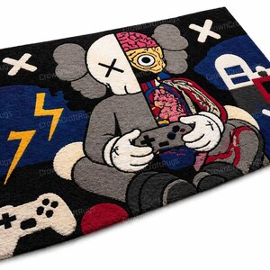 May include: A rectangular rug featuring a cartoon character with a split skull revealing the brain and internal organs, holding a game controller. The rug has a black background with blue, red, and yellow accents, including lightning bolts and a game controller.
