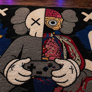 May include: A large, colorful rug featuring a split design of a cartoon character. One side is a skull with an X for eyes, the other side shows internal organs. The character is holding a game controller. The rug has a black background with white X's and other graphic elements.