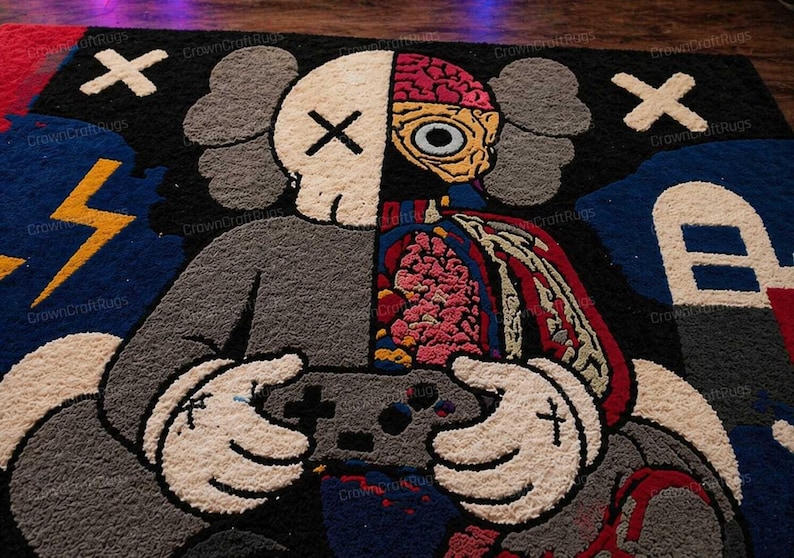 May include: A large, colorful rug featuring a split design of a cartoon character. One side is a skull with an X for eyes, the other side shows internal organs. The character is holding a game controller. The rug has a black background with white X's and other graphic elements.