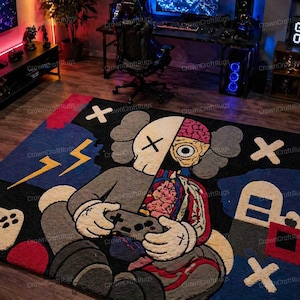 May include: A large, rectangular rug with a cartoon character design. The rug features a figure holding a game controller, with a split design showing internal anatomy. The color palette includes black, gray, blue, red, and yellow accents. The rug is designed for a gaming room.