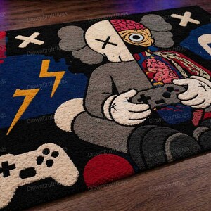 May include: A large, rectangular rug featuring a cartoon character holding a video game controller. The character is gray with white gloves and a partially exposed brain. The rug has a black, blue, and red color scheme with lightning bolt and controller graphics.