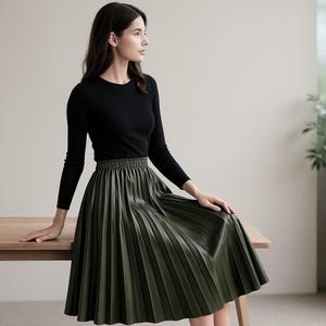 May include: A woman wearing a black long-sleeve shirt and an olive green pleated skirt. The skirt has a wide elastic waistband and falls to the mid-calf. The outfit is simple and elegant.