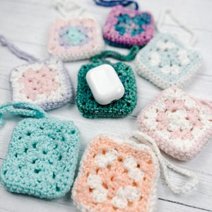 May include: A collection of colorful, crocheted square pouches, each with a loop for hanging. One pouch holds a white wireless earbud case. The pouches are in various pastel colors, including pink, blue, and green, with white accents.