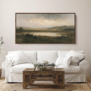 May include: A rectangular landscape painting in a dark wood frame depicting a calm lake surrounded by rolling hills under a cloudy, overcast sky. The foreground features dark green grasses and reeds, while the distant horizon shows soft, muted earth tones.
