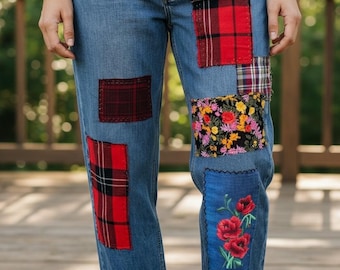 May include: Blue denim jeans featuring a patchwork design with various fabric patches. Patches include red and black tartan, floral, and embroidered red flowers. The jeans have a straight leg fit.