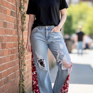 May include: Light blue denim jeans with distressed details and floral patterned side panels. The jeans have ripped sections and are paired with a black t-shirt and white sneakers. The outfit is casual and stylish.