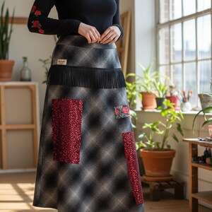 May include: A long black-sleeved top with red rose embroidery and a plaid skirt with red sequin patches and fringe. The skirt has a floral patch and is paired with burgundy boots. The outfit is suitable for a casual or semi-formal occasion.