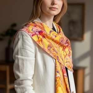 May include: A vibrant, patterned scarf in shades of yellow, orange, and purple is draped over a white blazer. The scarf's design features a swirling, abstract pattern. The woman is wearing a white blazer.
