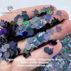 Op de afbeelding: Holografische zwarte glittervormen in de vorm van een handgebaar. De glitter is in verschillende tinten zwart, grijs en iriserende kleuren. De tekst "Figuratively Speaking - Holographic Black (8mm) Glitter Shapes" is zichtbaar.