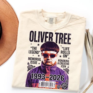 May include: A cream-colored t-shirt featuring a graphic print of Oliver Tree with red sunglasses and a bowl cut. The text reads OLIVER TREE, THE LEGEND, LIFE ROLLS ON, MEMORIAL ISSUE, HONORING A CREATIVE ICON, 1993-2026, REST IN PEACE, and BOOTLEG LEGACY.