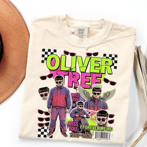 May include: A cream-colored t-shirt featuring a graphic print of Oliver Tree. The design includes the text OLIVER TREE, MISS YOU, and FOREVER WEIRD, along with multiple images of the artist, sunglasses, checkered patterns, and a barcode.