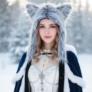 May include: A woman wearing a gray faux fur wolf hat with pointed ears. She is also wearing a white corset, a blue cape with white trim, and a lace top. The background is a snowy forest.