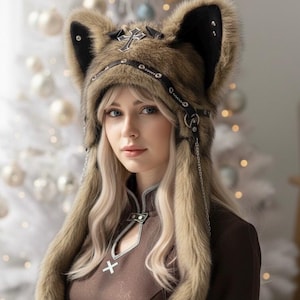 May include: A brown faux fur hat with large, upright ears and a decorative cross emblem. The hat features a leather band with metal studs and dangling chains. The hat is part of a costume or fashion accessory.