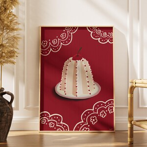 May include: A framed art print featuring a stylized illustration of a dessert. The artwork showcases a cream-colored cake with red accents and a cherry on top, set against a deep red background. Decorative white lace-like patterns frame the image.