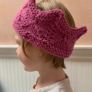 Könnte beinhalten: Ein rosa gestricktes Kronen-Stirnband mit einer spitzen Spitze und einem gewellten Rand.