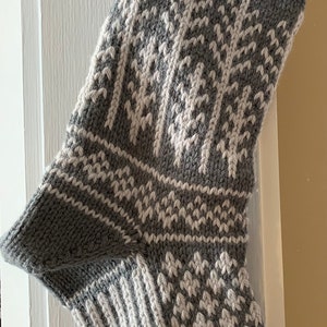 May include: A gray and white knitted Christmas stocking with a wintery design featuring trees.