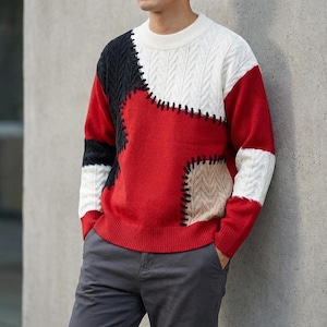 Puede incluir: Un suéter de bloques de color con un diseño de patchwork. El suéter presenta una combinación de paneles rojos, blancos, negros y beige, con costuras visibles. El suéter tiene cuello redondo y mangas largas.