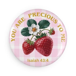 Könnte beinhalten: Ein runder Button mit rosa-weißem Vichy-Muster und dem goldenen Text "YOU ARE PRECIOUS TO ME". Der Button zeigt eine Erdbeerpflanze mit roten Erdbeeren, grünen Blättern und einer weißen Blüte. Der Text "Jesaja 43:4" ist ebenfalls enthalten.