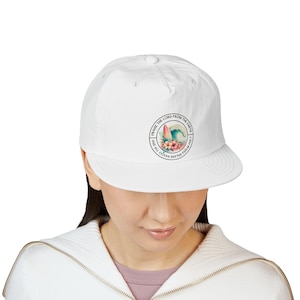 Puede incluir: Gorra de béisbol blanca con un diseño circular que presenta una tabla de surf, una ola del océano y flores. El texto alrededor del diseño dice "PRAISE THE LORD FROM THE EARTH AND ALL OCEAN DEPTHS PSALM 148:7".