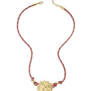 Könnte beinhalten: Halskette mit goldfarbenem Sonnenanhänger und rot-weißem Seilband. Der Sonnenanhänger hat detaillierte Gesichtszüge und Strahlen. Die Halskette hat einen Karabinerverschluss und eine Verlängerungskette.