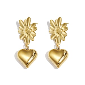 Könnte beinhalten: Ein Paar goldfarbene Ohrringe. Jeder Ohrring hat ein gänseblümchenförmiges Oberteil und einen herzförmigen Anhänger. Die Ohrringe sind aus glänzendem, reflektierendem Metall gefertigt und vor weißem Hintergrund dargestellt.