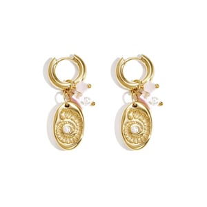 Könnte beinhalten: Goldfarbene Creolen mit ovalen Anhängern. Jeder Anhänger hat ein detailliertes Design mit einer zentralen Perle und ist mit rosa und weißen Perlen akzentuiert. Die Ohrringe sind für durchbohrte Ohren konzipiert.