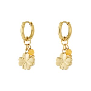 Könnte beinhalten: Ein Paar goldfarbene Creolen. Jeder Ohrring hat einen vierblättrigen Kleeblatt-Anhänger und kleine gelbe Perlen. Die Ohrringe sind mit einer polierten Oberfläche versehen, die das Licht reflektiert.