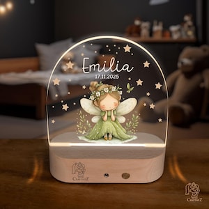 A wooden nightstand with a glass display case on it, featuring a fairy with wings and a flower crown. The fairy is surrounded by stars and the name "Emilia" is written above her.