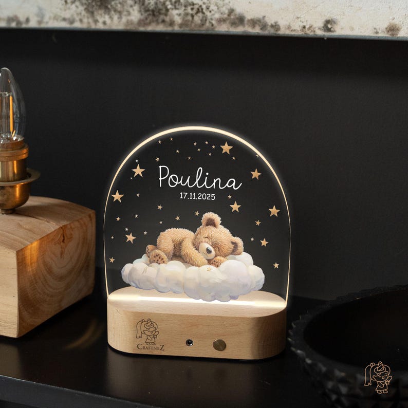 A wooden nightstand with a teddy bear on a cloud illuminated by a light, and the name "Poulina" written on it.